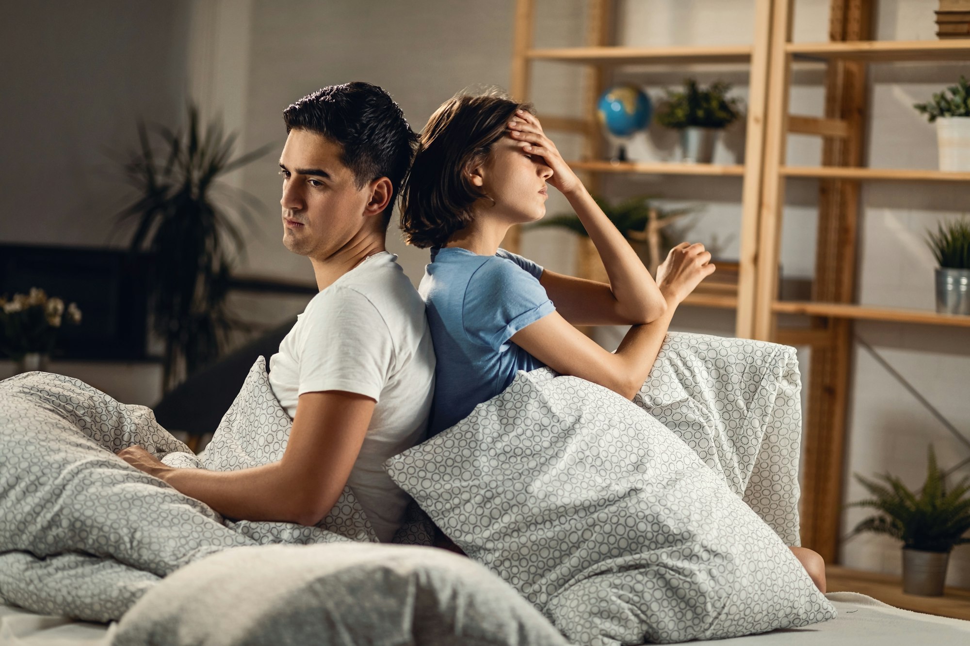 Displeased couple sitting back to back on the bed.