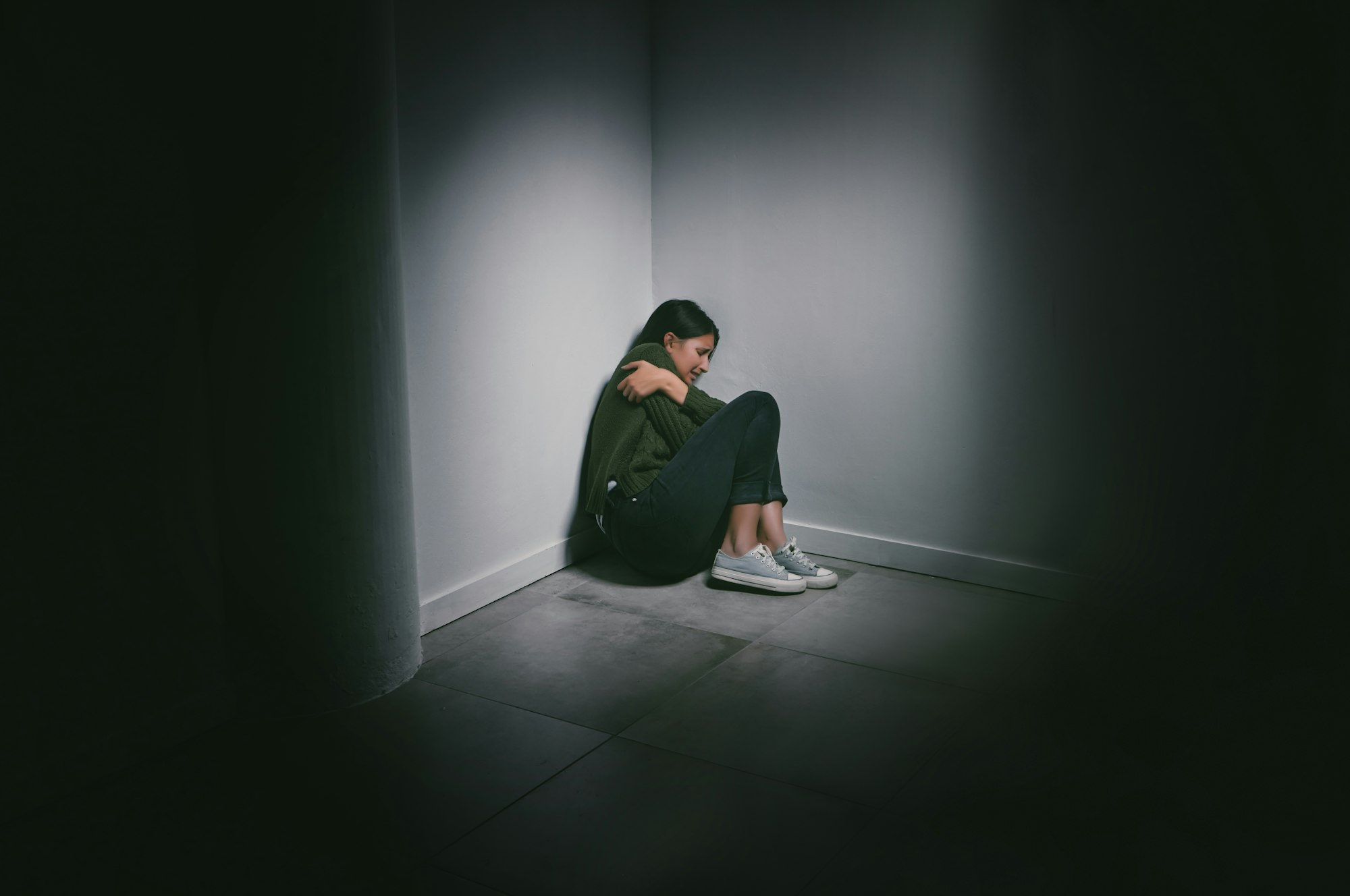 Where is everyone when you need them. Shot of a young woman sitting in the corner of a dark room.